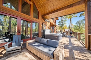 A covered deck with a wicker sofa, a grill, and a view of the surrounding trees. - Llama Creek Cabin at Eagles Nest (Banner Elk)