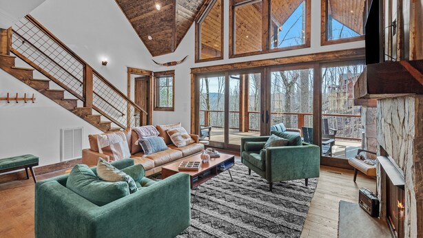 A spacious living area with a high ceiling, large windows, a fireplace, and a staircase. - Llama Creek Cabin at Eagles Nest (Banner Elk)