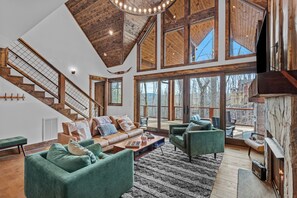 A spacious living area with a high ceiling, large windows, a fireplace, and a staircase. - Llama Creek Cabin at Eagles Nest (Banner Elk)