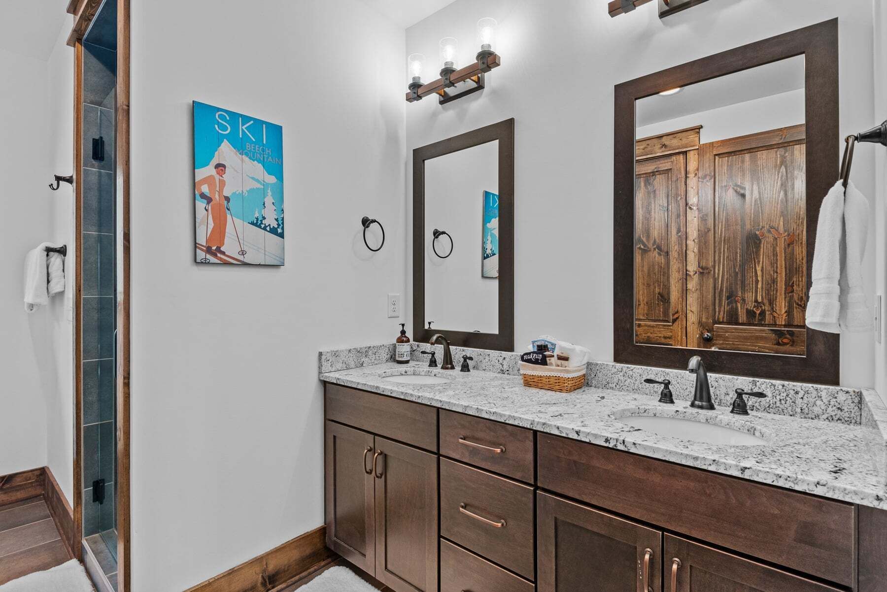 Une salle de bain avec un grand miroir, un lavabo doté d’un plan de travail en marbre, des meubles en bois et une affiche représentant une station de ski.