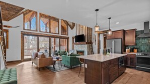 A spacious kitchen with a large island, wooden cabinetry, and a stone fireplace. - Llama Creek Cabin at Eagles Nest (Banner Elk)