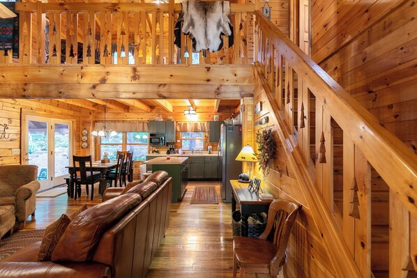 A wooden cabin interior with a dining area, kitchen, and a staircase.