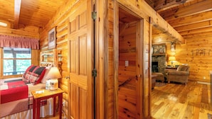 Interior de cabana de madeira com uma cama, uma mesa com abajur, lareira e um sofá.