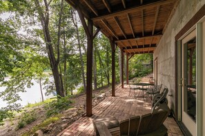 A covered patio with outdoor furniture, a view of a lake, and trees in the background.