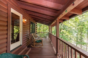 A wooden porch with a rocking chair and a table, overlooking a forest. - Garretts Getaway at Watauga Lake (Butler)