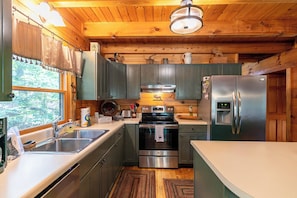 A kitchen with wooden cabinets, stainless steel appliances, and a window with a view of trees. - Garretts Getaway at Watauga Lake (Butler)
