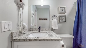 Ein Badezimmer mit Marmorwaschtisch, Toilette in Weiß, einem an der Wand befestigten Föhn, einem Handtuchhalter und einem gerahmten Bild.