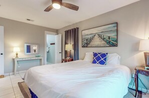 Ein Schlafzimmer mit einem Bett, einem Schreibtisch, einem Stuhl, einer Lampe, einem Deckenventilator und einem Bild an der Wand.