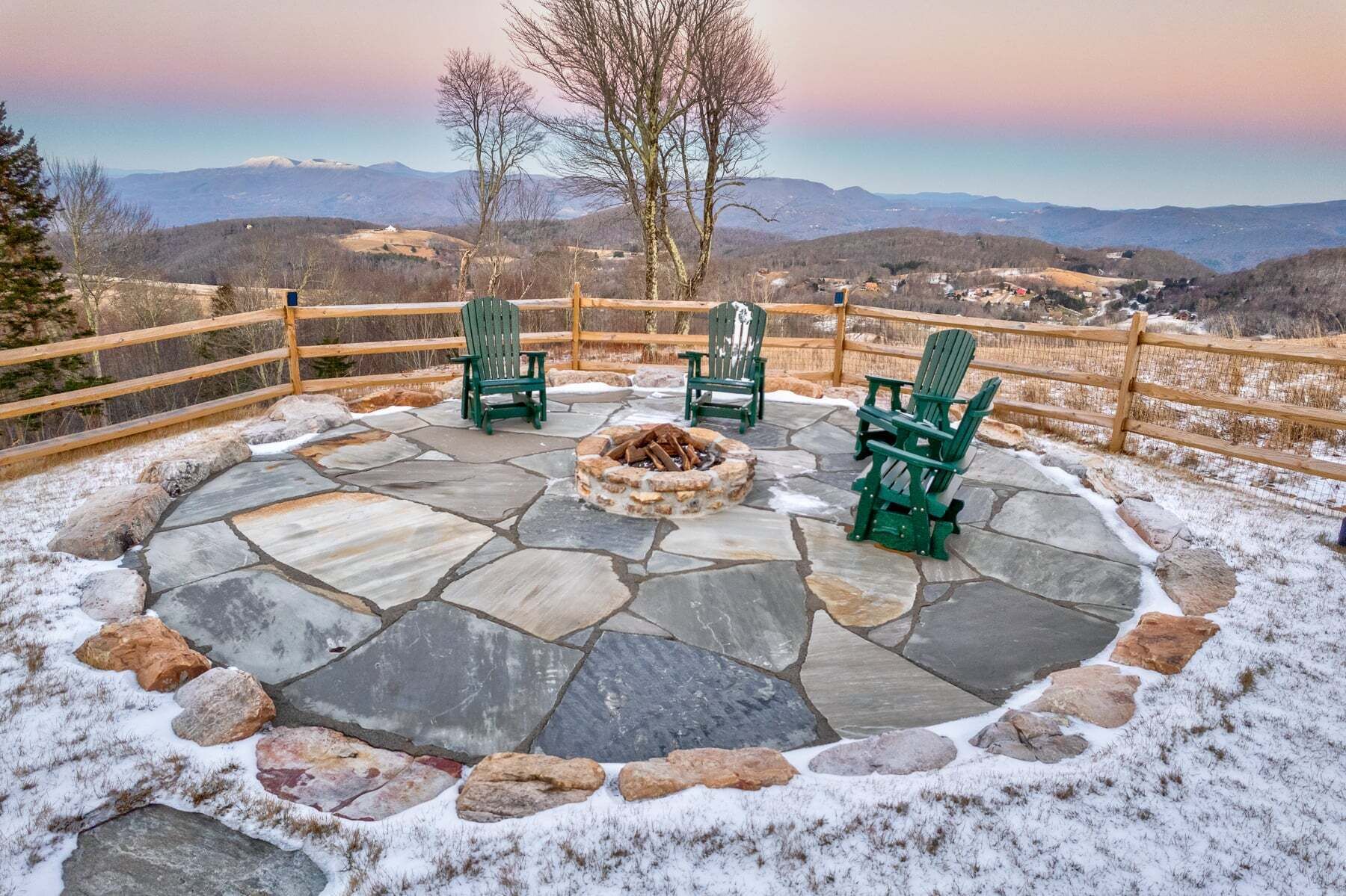 A stone fire pit with chairs and a wooden fence overlooking a mountainous landscape.