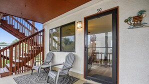 A covered porch with a wooden staircase, two Adirondack chairs, a small table, and a welcome mat. - Holiday Hideaway - Sand Castle Villas #30 (Panama City Beach)