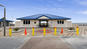 A beachside building with a blue roof, a covered entrance, and a paved walkway leading to it. - Holiday Hideaway - Sand Castle Villas #30 (Panama City Beach)