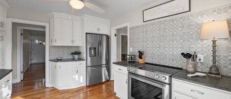 A modern kitchen with white cabinetry, stainless steel appliances, and a wooden floor.