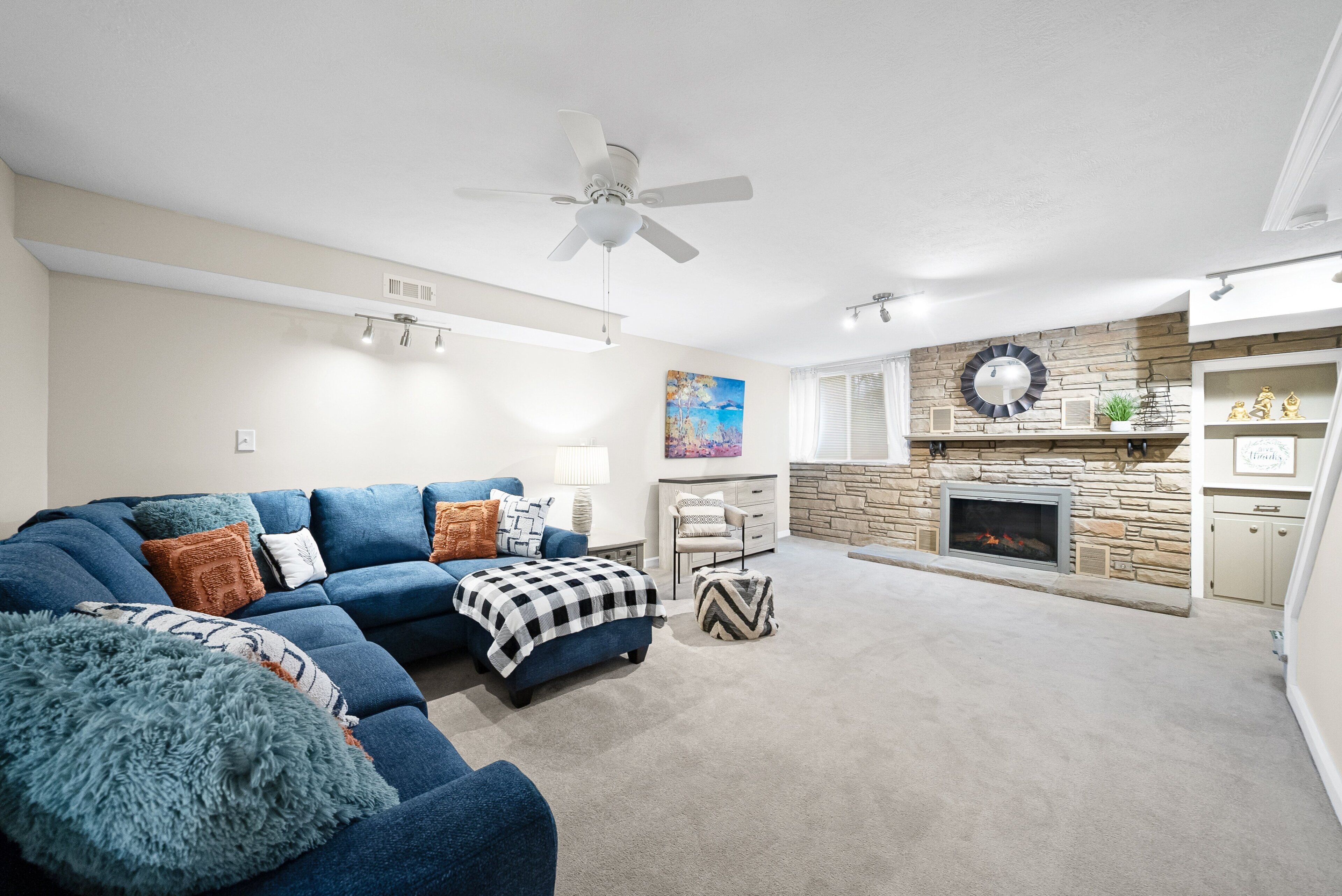 A living room with a blue sectional sofa, a fireplace, and a ceiling fan.