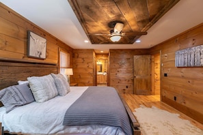 Ein schlicht eingerichtetes Schlafzimmer im Chalet-Stil mit Bett, Kissen, Deckenventilator und einer Tür zum Badezimmer.