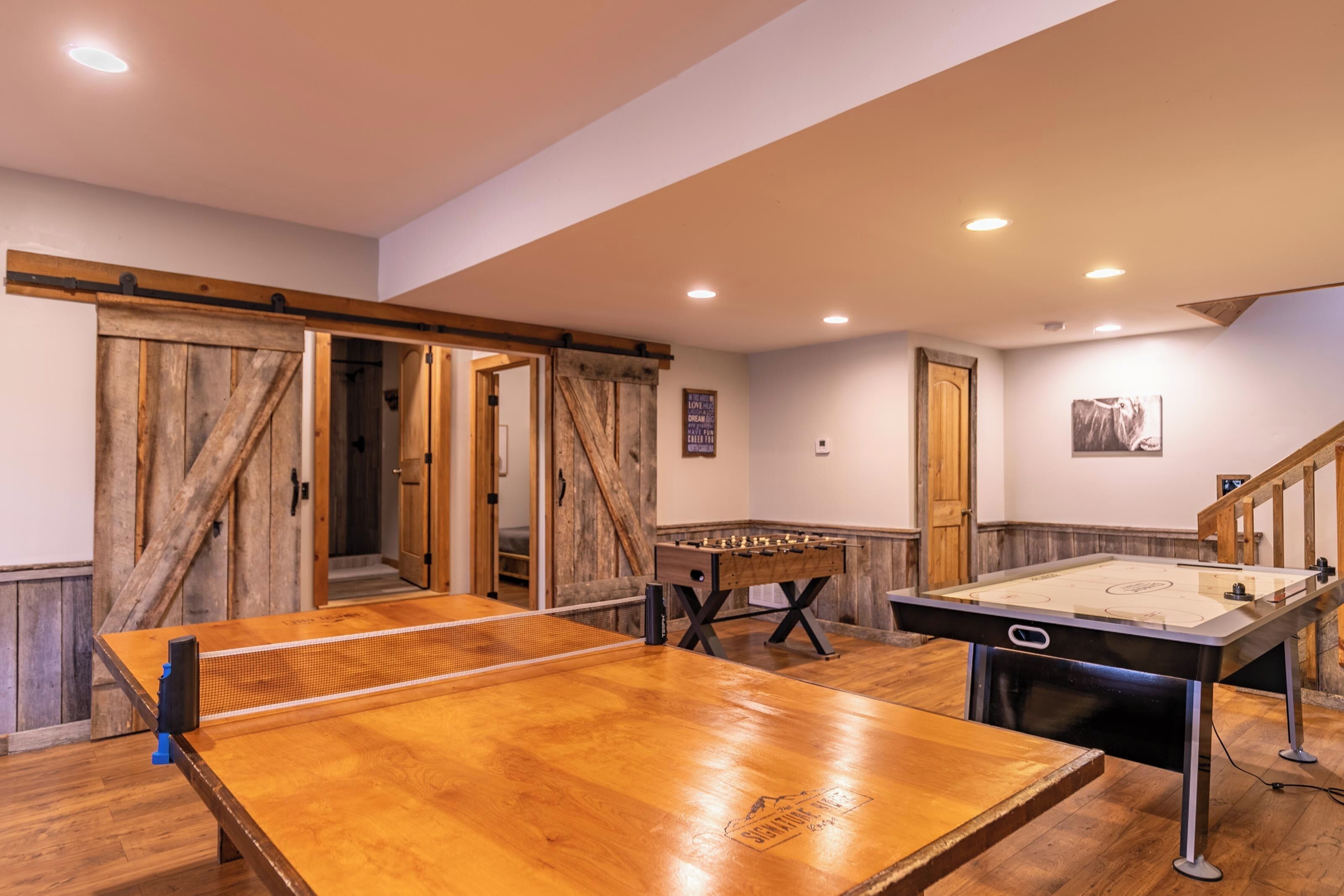 A room with a ping pong table, foosball table, and a wooden door.