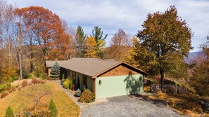 Ein rustikales Blockhaus mit geneigtem Dach, umgeben von Herbstlaub und einer Schotterauffahrt.