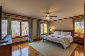 Ein Schlafzimmer mit einem großen Bett, Holzböden, einem Deckenventilator und Fenstern mit Vorhängen.