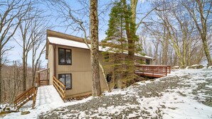 Uma cabana com escada de madeira, um deck e vista para a floresta ao redor.