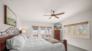 Quarto com cama, ventilador de teto, janela com vista e porta para o exterior.
