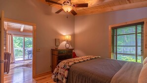 Ein Schlafzimmer mit einem Bett, einem Deckenventilator, einem Nachttisch mit Lampe, einem Fenster mit Jalousien und einer Tür, die zu einem Außenbereich führt.