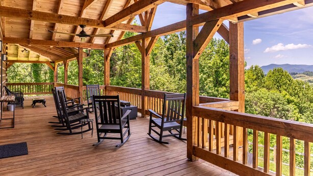 Eine Holzterrasse mit Schaukelstühlen und einem Tisch, mit Blick auf eine bewaldete Landschaft.