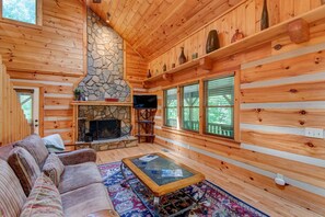 A log cabin interior with a stone fireplace, wooden walls, a sofa, and a television. - Little Creek Lodge (Vilas)