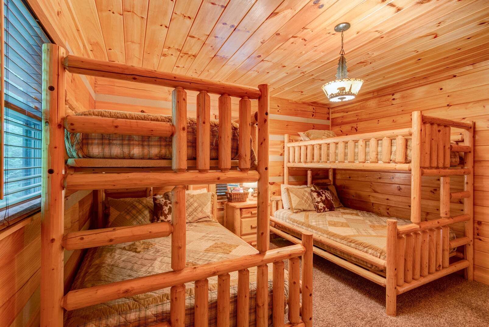 A wooden cabin interior with bunk beds, a chandelier, and a window with blinds.