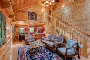 A log cabin interior with a wooden staircase, a dining area, and a living room with a patterned rug. - Little Creek Lodge (Vilas)