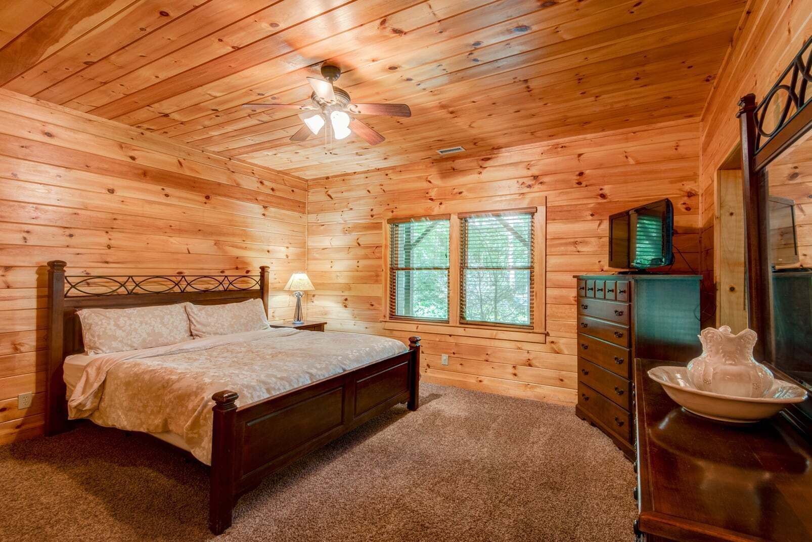 A wooden cabin bedroom with a bed, dresser, and window.
