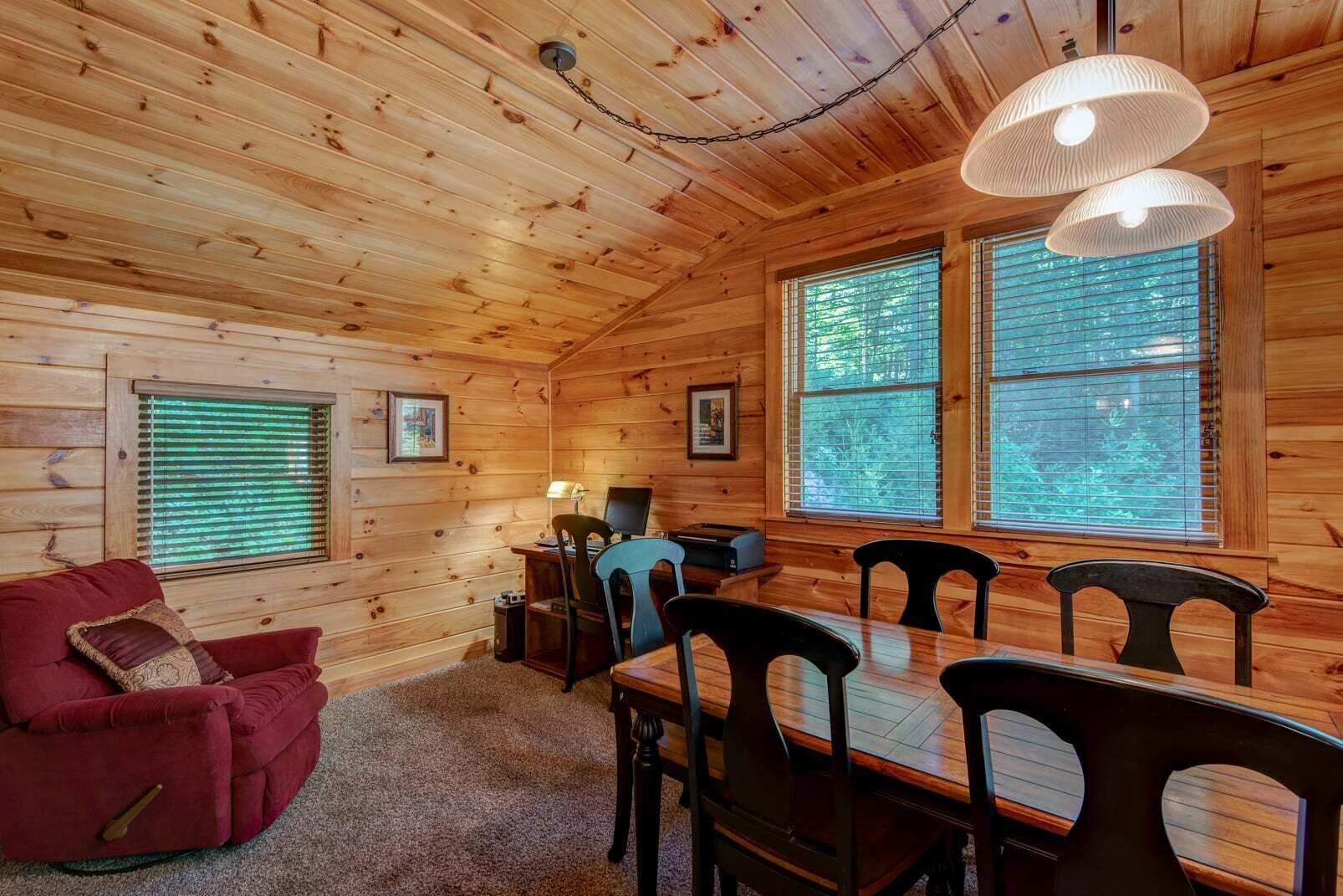 Ein Holzblock-Innenraum mit einem Esstisch, Stühlen, einem roten Sofa und zwei Fenstern mit Jalousien.
