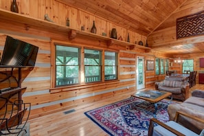 A log cabin interior with a large window, a television, a sofa, and a rug. - Little Creek Lodge (Vilas)