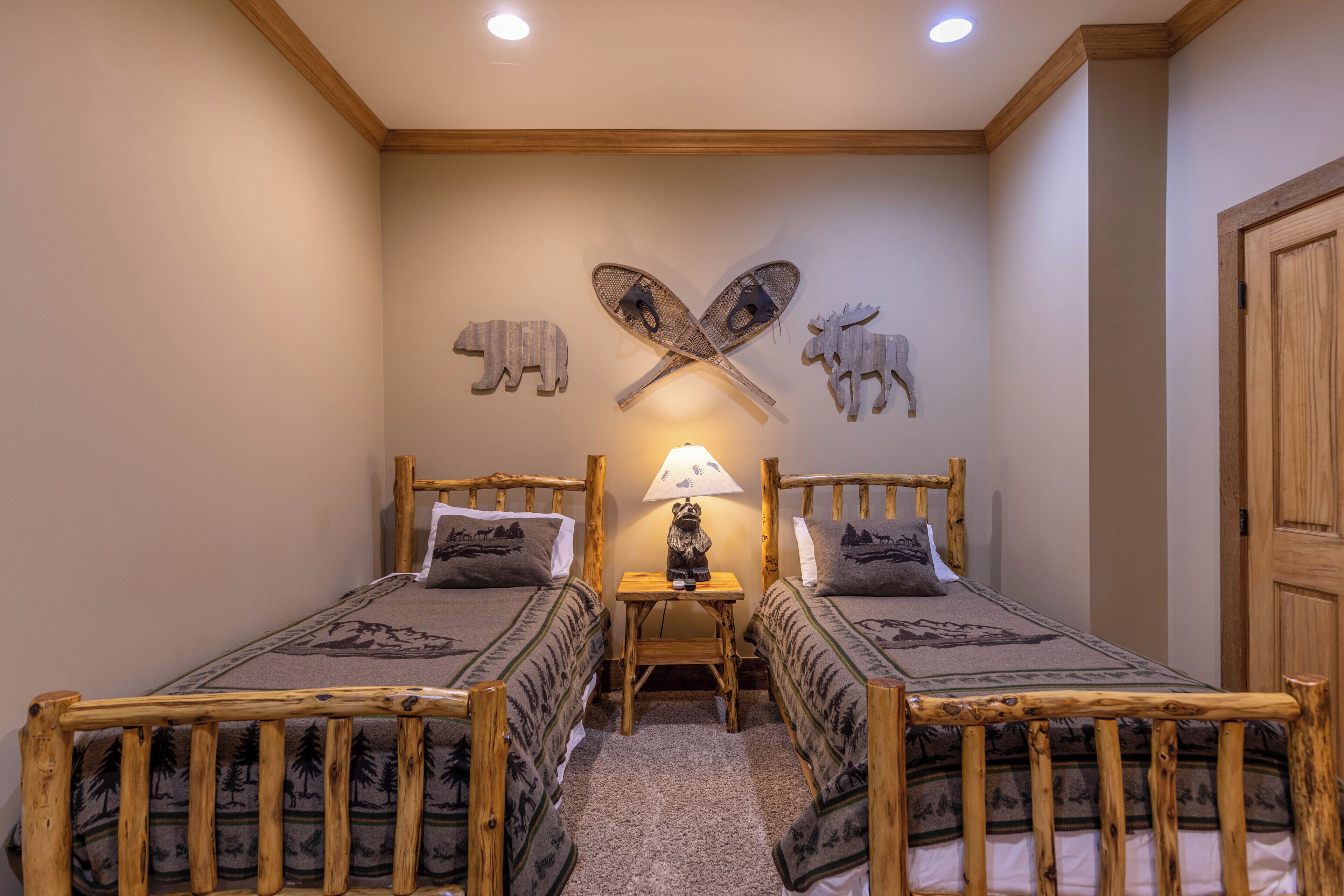 Ein Zimmer mit zwei Holzbetten, einem kleinen Tisch mit Lampe und Tierdarstellungen an der Wand.