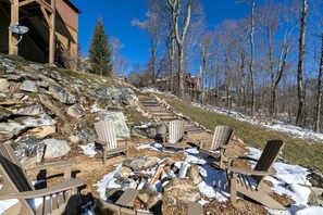 Eine Holzterrasse mit Adirondack-Stühlen, einer Steinkaminanlage und einem Gebäude mit Satellitenschüssel.