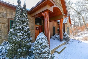 Ein Holzhaus mit Veranda, schneebedeckten Bäumen und einer Steintreppe, die zum Eingang führt.
