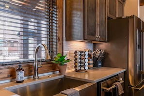 A kitchen with a stainless steel sink, wooden cabinets, a built-in stove, and a window with blinds. - Green Valley III at Eagles Nest (Banner Elk)