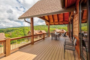 A wooden deck with outdoor furniture, a covered area, and a view of a forested landscape. - Green Valley III at Eagles Nest (Banner Elk)