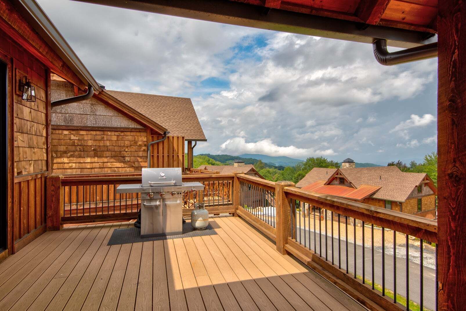 A wooden deck with a grill and gas tank, overlooking a residential area with houses and mountains.