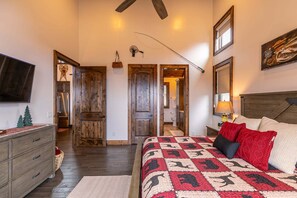 A bedroom with a large bed, wooden doors, a television, and a painting on the wall. - Green Valley III at Eagles Nest (Banner Elk)