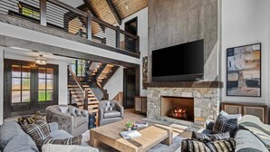 A spacious living area with a stone fireplace, leather sofas, and a large flat-screen TV. - One More Day at Eagles Nest (Elk Park)
