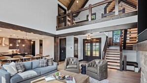 A spacious living area with a high ceiling, a dining area, and a staircase leading to an upper level. - One More Day at Eagles Nest (Elk Park)