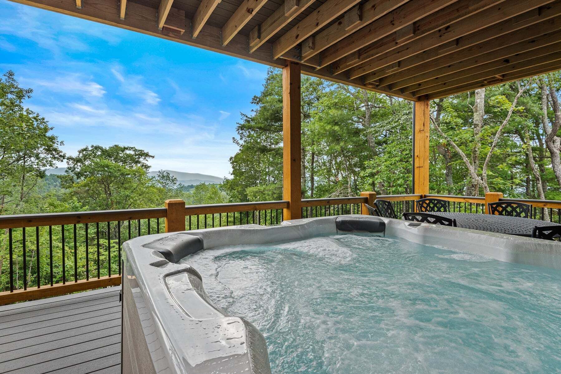A hot tub on a wooden deck with a view of trees and hills.