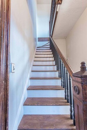 A wooden staircase with a handrail and a wall-mounted light switch.