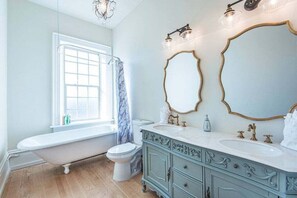 A bathroom with a freestanding bathtub, a toilet, a vanity with a sink, and two mirrors.