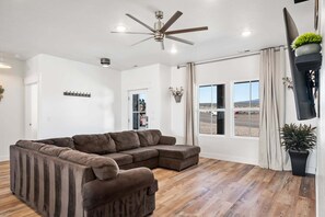 A living room with a sectional sofa, a ceiling fan, a large window with a view, and a mounted TV. - 405 Aspen Valley - Panguitch (Panguitch)