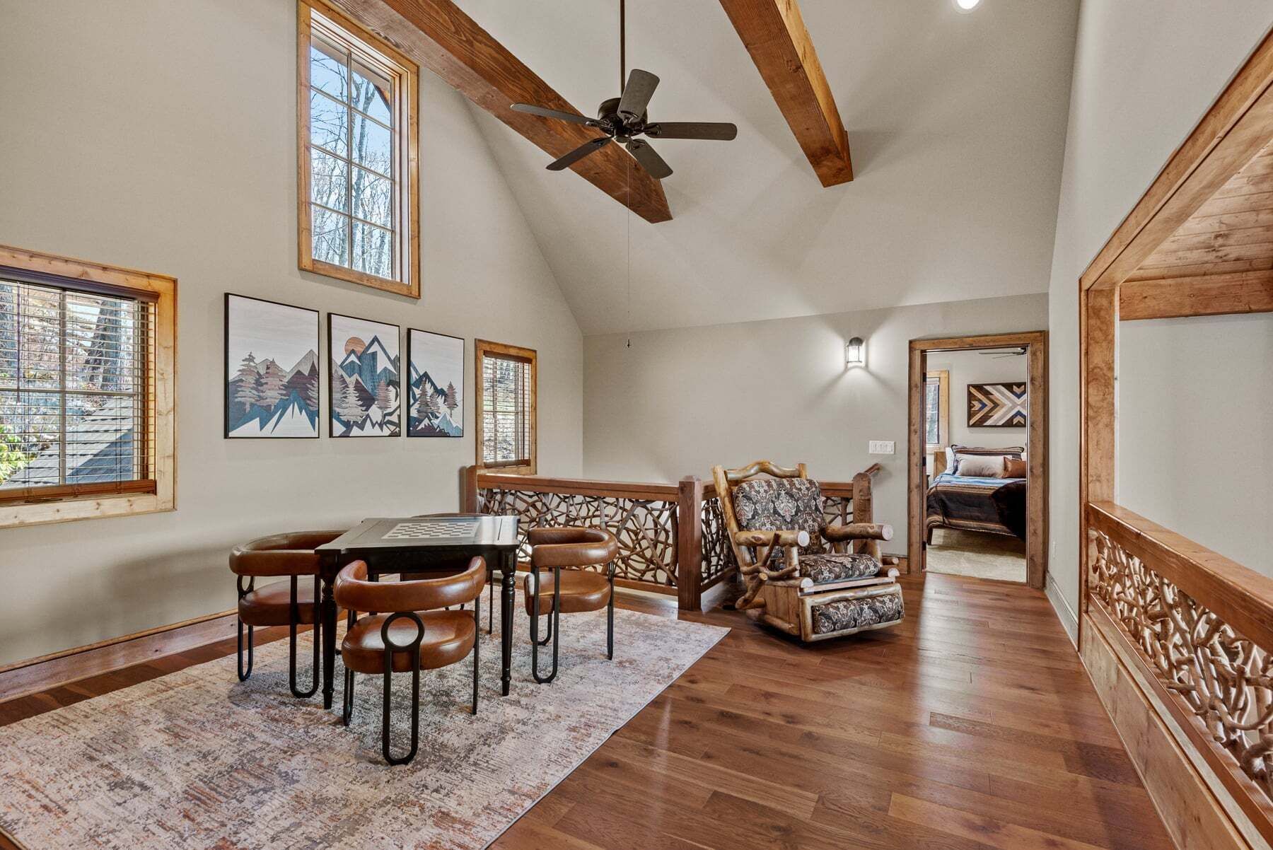 A spacious loft with a high ceiling, wooden beams, a dining area with a table and chairs, and a view through an open doorway to a bedroom.