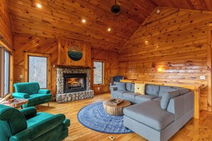 A log cabin interior with a fireplace, two sofas, and a round rug.