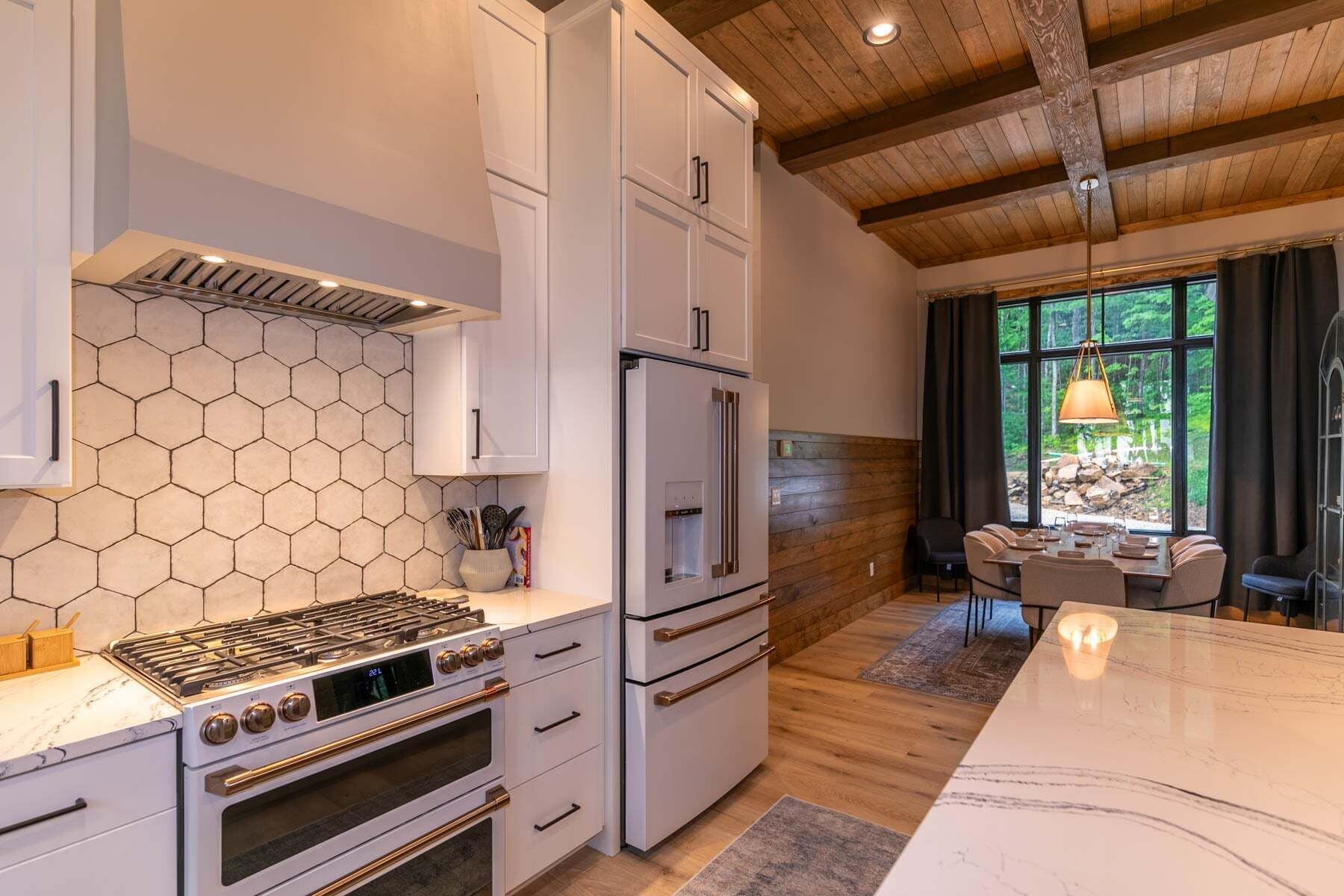 Eine moderne Küche mit Gasherd, Backofen und Kühlschrank, Holzboden und einem Essbereich mit Blick ins Freie.
