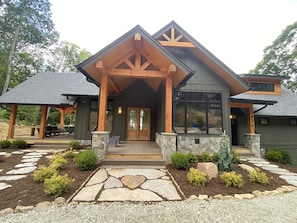 A modern house with a stone entrance, wooden porch, and a large window. - The Heartstone Lodge at Eagles Nest (Elk Park)