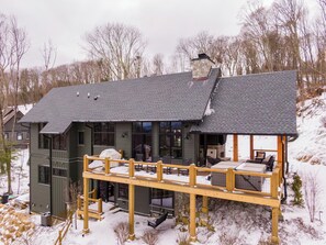 A two-story house with a covered deck, a stone chimney, and a large window. - The Heartstone Lodge at Eagles Nest (Elk Park)