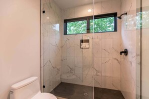 A modern bathroom with a glass-enclosed shower, a toilet, and a window providing a view of greenery. - The Heartstone Lodge at Eagles Nest (Elk Park)